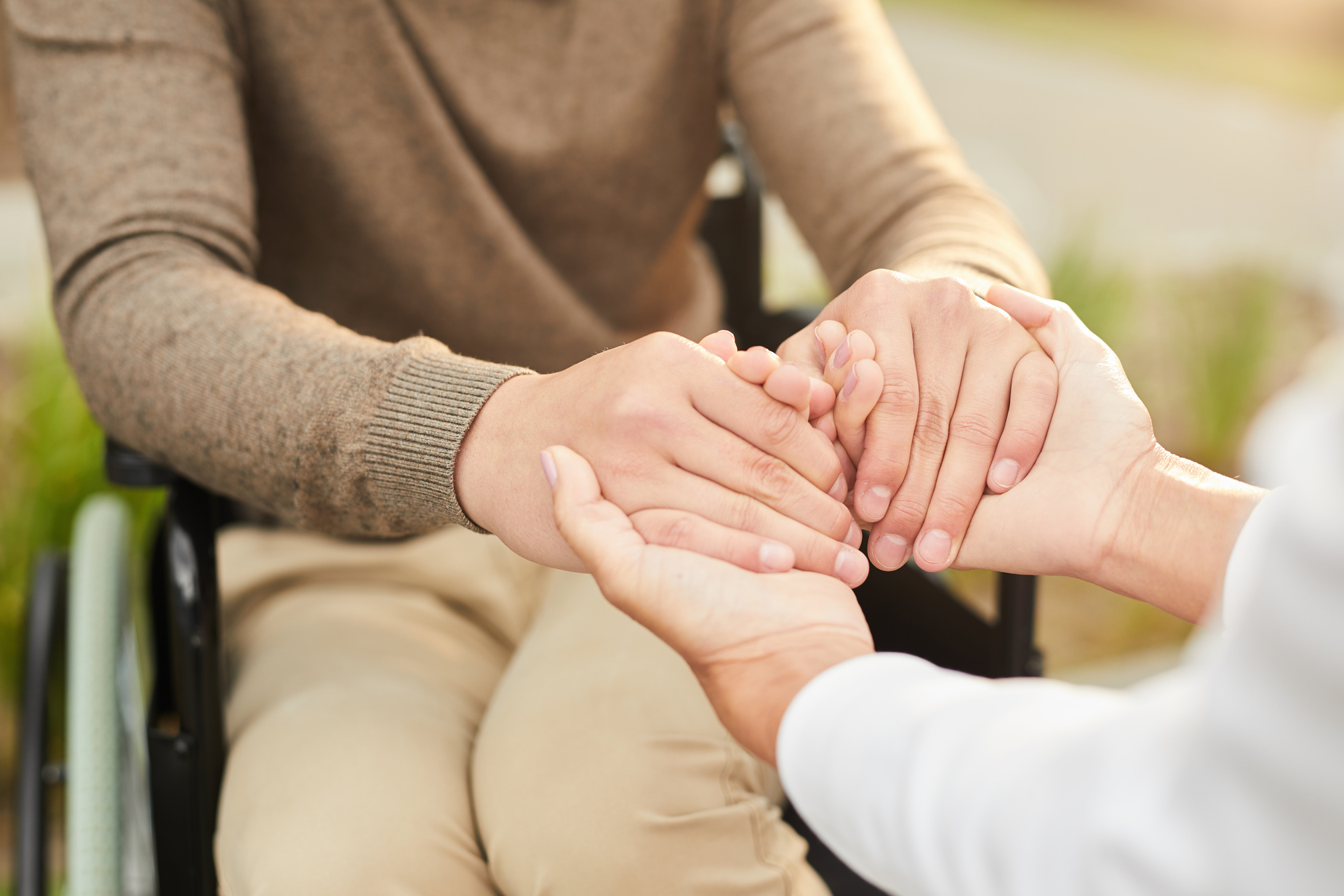 Close-up of unrecognizable social care worker and disabled patient in wheelchair holding hands